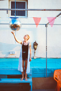 Woman reaching for disco ball hanging against wall