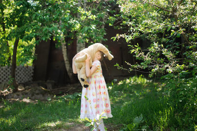 Cute european kid girl in dress with soft big toy dog in backyard, in park summer