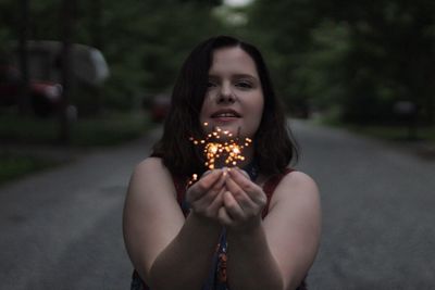Portrait of beautiful young woman with sparklers on road