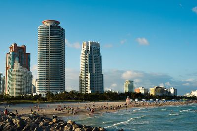 People at beach by city against sky