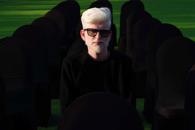 Portrait of the albino man sitting on the black chair wearing glasses