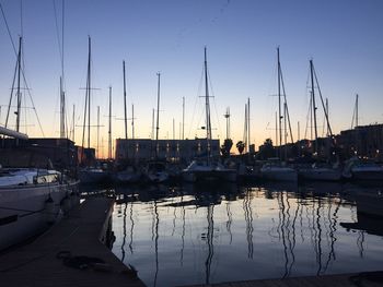 Sailboats moored in harbor at sunset