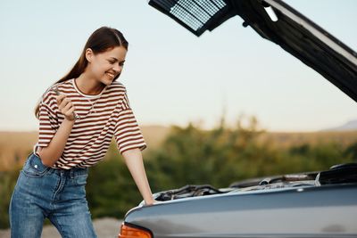 Portrait of smiling young woman standing against car