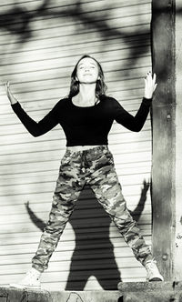 Smiling teenage girl standing against wall during sunny day