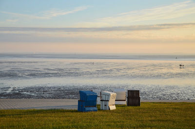 Hooded chairs on beach against sky during sunset