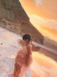 Woman standing on rock against sky during sunset