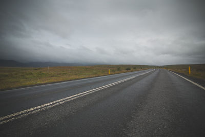 Empty road amidst field against cloudy sky