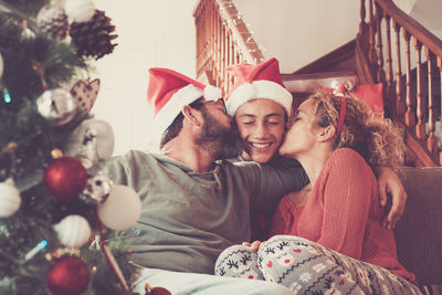 Father and mother kissing son while sitting by christmas tree at home