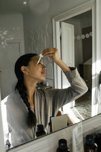 Young woman applying cream on face