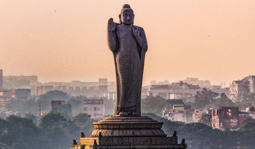 Buddha statue in city against clear sky during sunset