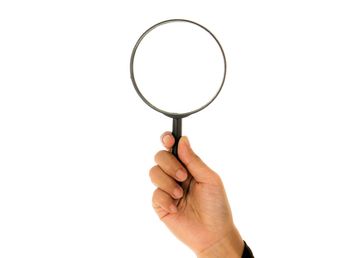 Cropped hand of woman holding magnifying glass against white background