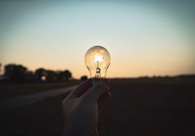 Cropped hand of person holding light bulb against sky