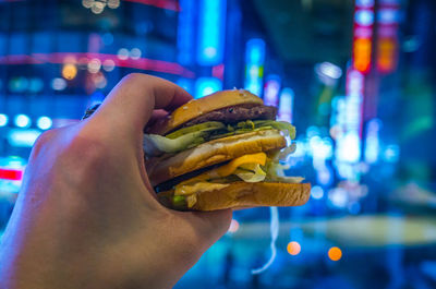 Cropped hand having burger in illuminated city at night