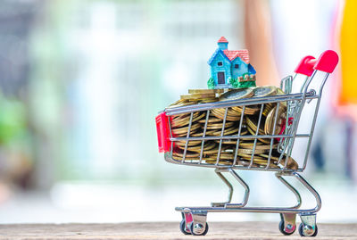 Close-up of coins and house model in shopping cart on table