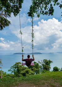 Rear view of woman sitting on swing against sky