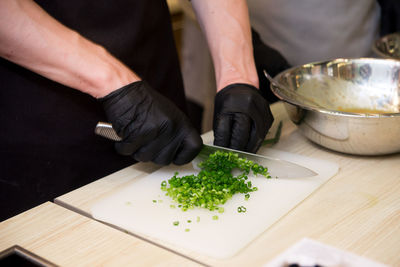 Chef's hands in black gloves chopping greens on board, cooking process