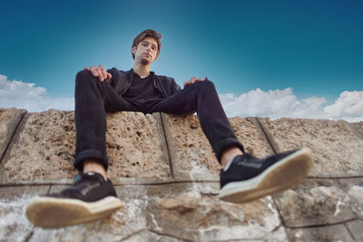 Low angle view of man sitting on rock against sky