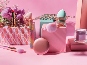 Make up tools, brushes, foundation egg, lipstic, nail polish products on geometric podiums on pink