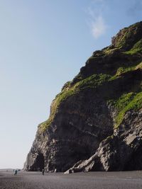 Low angle view of cliff by sea against clear sky