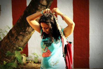 Smiling young woman wearing floral garland while standing against wall