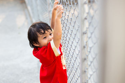 High angle view of playful boy holding chainlink fence