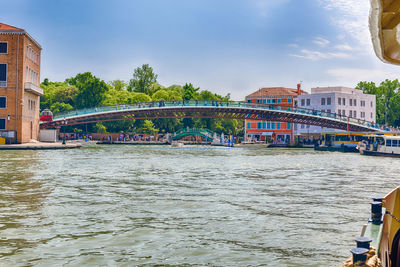 Bridge over river by buildings against sky