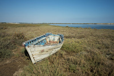 Abandoned rowboat moored on grassy seashore against clear blue sky