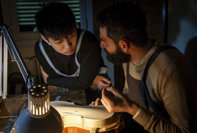 Pair of craftsmen violin maker while working on a new violin in the workshop