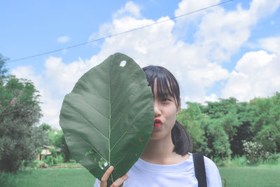 Young woman holding leaf against sky