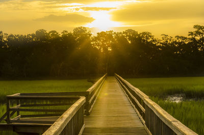 Walkway by lake against sky during sunset