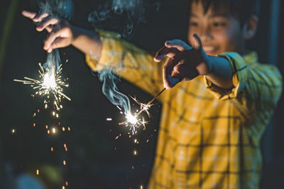 Midsection of boy holding sparkler at night