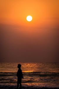 Silhouette man standing at beach against sky during sunset