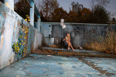 Young woman sitting by balloons on chair against wall
