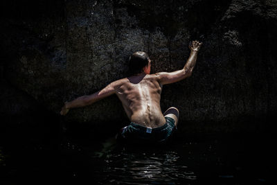 Rear view of shirtless man climbing on concrete retaining wall