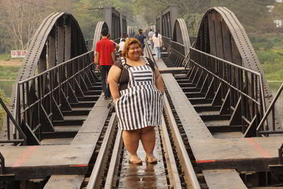 Portrait of overweight woman standing amidst railroad track on bridge