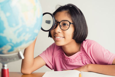 Girl looking at globe through magnifying glass at desk