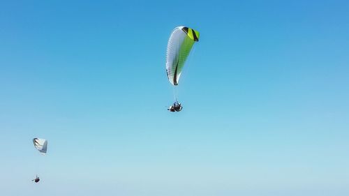 Low angle view of people paragliding against clear blue sky