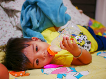 High angle view of boy drinking milk while lying on bed