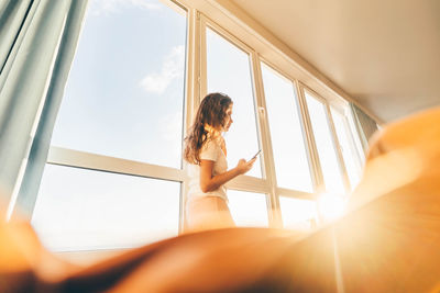 Low angle view of young woman looking through window