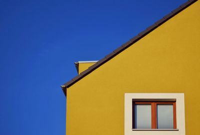 Low angle view of yellow building against clear blue sky