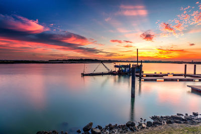 Pier on river against cloudy sky during sunset