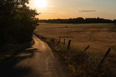 Road amidst field against sky during sunset