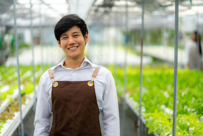 Portrait of smiling young woman standing against fence