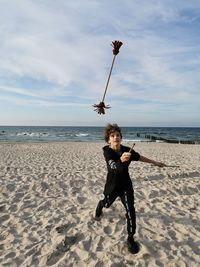 Man with arms raised on beach against sky, juggling