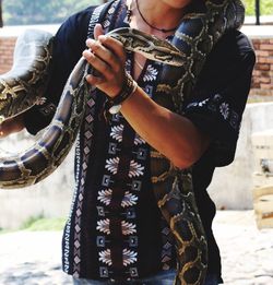 Midsection of man holding python while standing on field