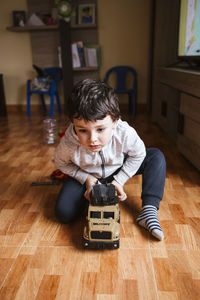 Positive little boy in casual clothes sitting on floor and playing toy truck while spending free time at home