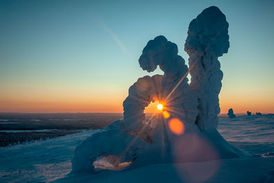 Snow covered field against sky during sunset