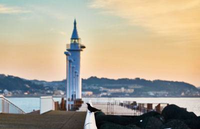 Lighthouse by sea against sky during sunset