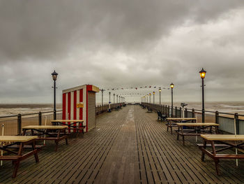Empty footpath by street lights against sky