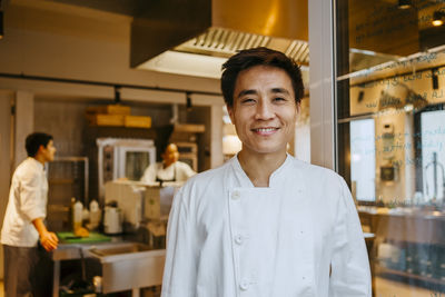 Portrait of happy male chef standing at door in commercial kitchen
